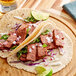 Eat Meati plant-based carne asada steak in two tacos with meat and vegetables on a wooden plate.