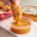 A hand holding a fried chicken stick over a container of Ken's Foods Chick'n Dip'n Sauce.