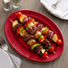 A Tuxton cayenne oval china platter with skewers of meat and vegetables.