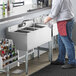 A man in a red apron using a Regency stainless steel 3 compartment underbar sink.