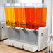 A Crathco refrigerated beverage dispenser with three clear containers of orange liquid.