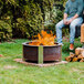 A couple of people sitting on chairs at a BREEO Corten Steel fire pit with a fire.