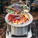 A BREEO stainless steel grill grate with meat cooking on a fire pit.