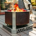 A BREEO stainless steel fire pit base with a fire in it on a deck.