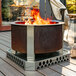 A BREEO Corten steel fire pit on a deck with a fire burning.