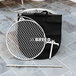 A BREEO stainless steel grill grate with a metal circle and handle next to a bag.