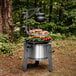 A Breeo stainless steel fire pit grill with meat and vegetables on it.