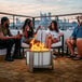 A group of people sitting around a BREEO stainless steel fire pit on an outdoor patio.