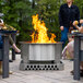 A group of people sitting around a BREEO stainless steel fire pit on an outdoor patio.