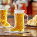 Two Acopa beer mugs filled with beer in the shape of boots on a table.