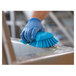 A hand in a blue glove using a Vikan blue brush to clean a metal surface.