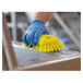 A person wearing blue gloves cleaning a metal surface with a Vikan yellow scrub brush.