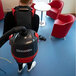 A person using a NaceCare red and black corded backpack vacuum cleaner.