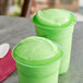 Two green frozen drinks made with Philadelphia Water Ice Sour Apple in plastic cups.