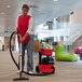 A woman using a NaceCare cordless canister vacuum to clean a carpet.