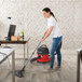 A woman using a NaceCare cordless canister vacuum to clean a carpeted floor.