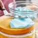 A bowl of Stratas Nutex Hi-Ratio Liquid Cake Shortening with blue frosting being spread on a cake with a knife.