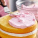 A person spreading pink frosting on a cake using a knife.