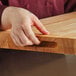 A person holding a Choice wood cutting board with rounded edges.