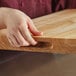 A person holding a Choice wood cutting board with rounded edges.