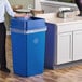 A woman standing next to a Lavex blue square recycling bin.
