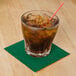 A glass with a straw and brown liquid with a Hoffmaster Hunter Green 2-Ply Beverage Napkin on the counter.