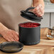 A hand using a black Planetary Design Airscape food container to store red grains.
