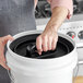 A hand inserting a black Planetary Design Airscape lid onto a white bucket.