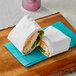 A sandwich wrapped in white paper with Bagcraft Dubl Shield sandwich wrap on a cutting board.