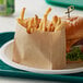 A Bagcraft natural paper bag with a cheeseburger and fries on a plate.