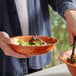 A person holding a wooden salad bowl filled with lettuce.