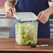 A person cutting a cucumber in an Araven food storage container on a counter.