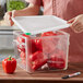 A person putting a plastic container of red bell peppers into an Araven square food storage container.