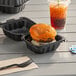 A cheeseburger and a drink in a black plastic hinged take-out container.