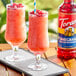 Two glasses of red pomegranate drinks with straws on a tray with a Torani bottle.