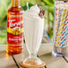 A milkshake in a glass with a straw and Torani Almond Roca flavoring syrup on a coaster.