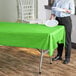 A woman standing at a table with a lime green plastic Table Mate tablecloth.