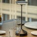 An Abert Tempo rechargeable table lamp on a table with black liquid in glasses.
