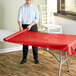 A woman rolling a red Table Mate plastic tablecloth.