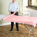 A woman rolling a pink plastic table cover onto a table.