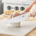 A person holding a Victorinox Chef Knife with a white handle cutting a piece of cheese.