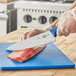 A person cutting meat on a cutting board with a Victorinox 10" Chef Knife with a blue handle.