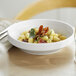 A close-up of a Libbey white porcelain coupe bowl filled with pasta and bacon.