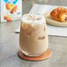 A box of Almond Breeze Unsweetened Vanilla Almond Milk on a table with a glass of iced coffee and a pastry.