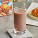 A glass of Almond Breeze chocolate almond milk on a coaster on a table next to a box of cookies.