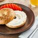 A bagel with Oatly plant-based cream cheese and strawberries on a plate.