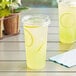 Two Choice clear plastic cups of lemonade with a lemon slice on a table.