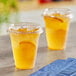 Two Choice clear plastic cups with orange juice and ice on a table.