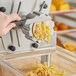 A hand using a black handled pasta machine to cut fusilli noodles.