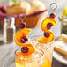 Two stainless steel skewers with orange slices and cherries on top.